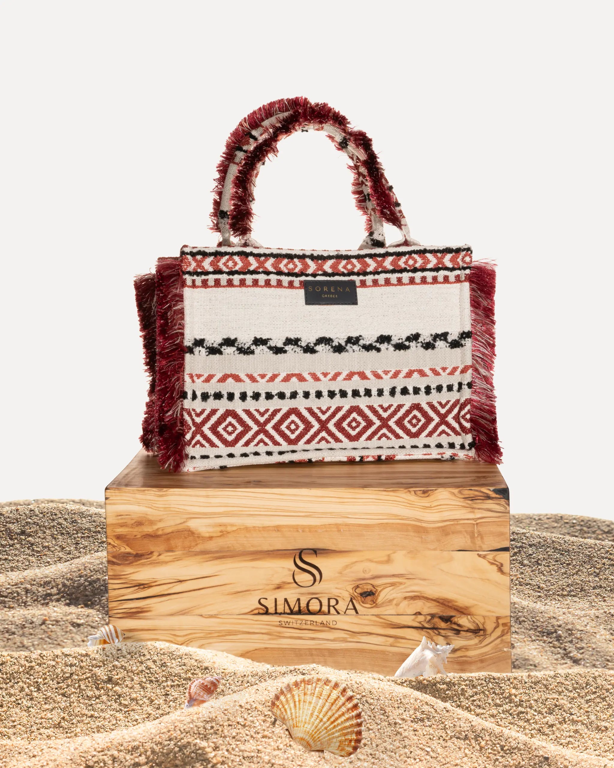 Frontansicht der Sorena Greece Large Tote Bag auf dem Olivenholzsockel von SIMORA– tribal-inspiriertes Muster in warmen Tönen, Fransen, Label und goldfarbene Details sichtbar, hochwertige shopper tasche damen schweiz mit Designfokus.
