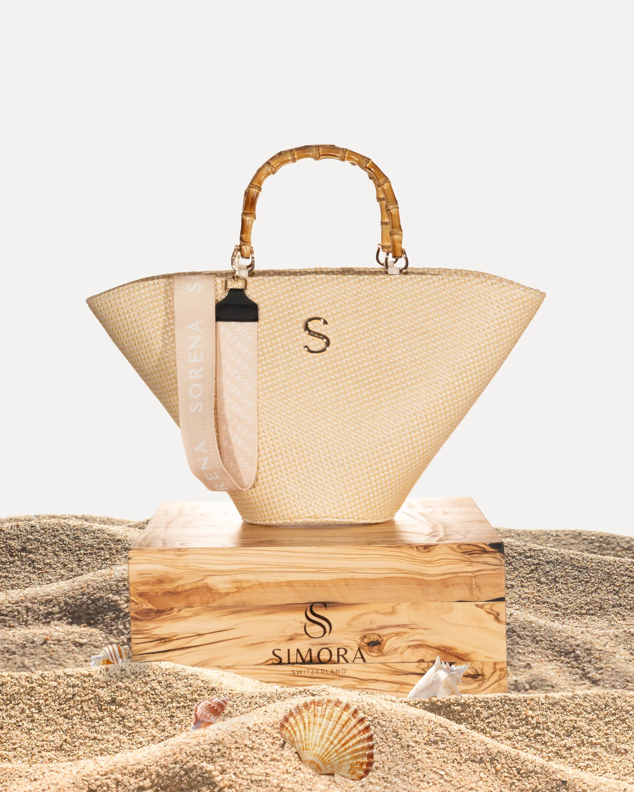 Sorena Greece Irida Medium Basket Bag auf SIMORA Olivenholzsockel, Frontansicht naturfarbenes Stroh Korbform warm handgefertigt Griechenland Strandtasche