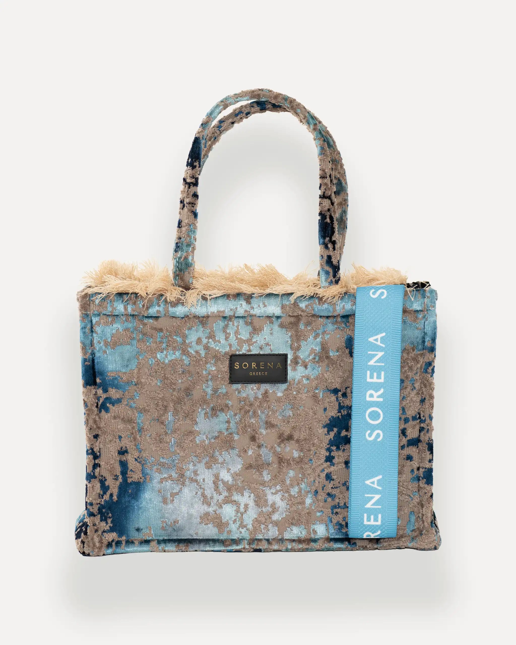 Frontansicht der Sorena Greece Medium Tote Bag – blau-beige-graues Muster, Fransen, Label und vertikales Branding sichtbar, hochwertige shopper tasche damen schweiz mit Designfokus.