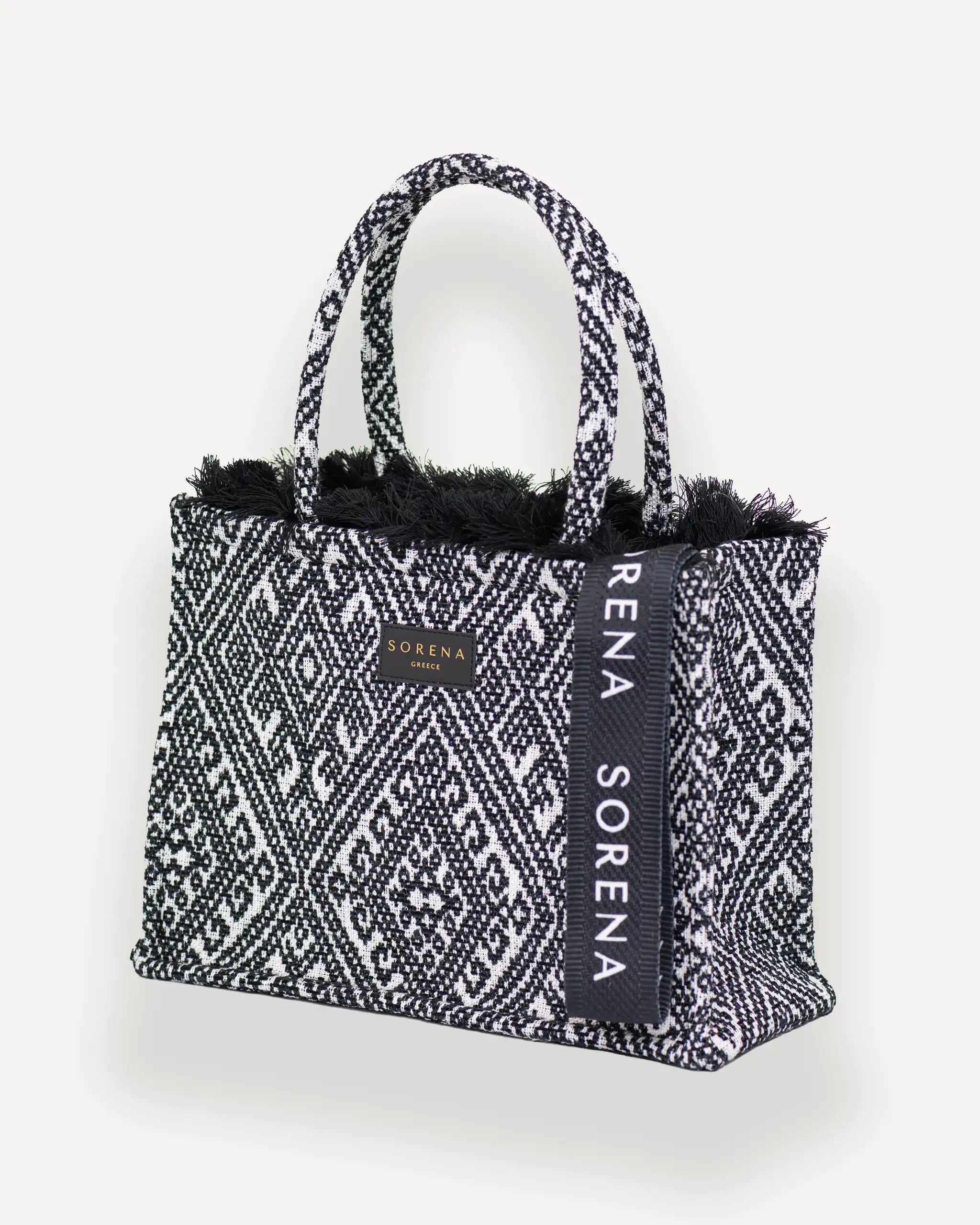 Sorena Greece Medium Tote Bag linksseitig getragen – elegante tote bag mit Fransen und vertikalem „SORENA“-Band, ideal als shopper bag für City-Looks, tote bag mit geometrischem muster schweiz.