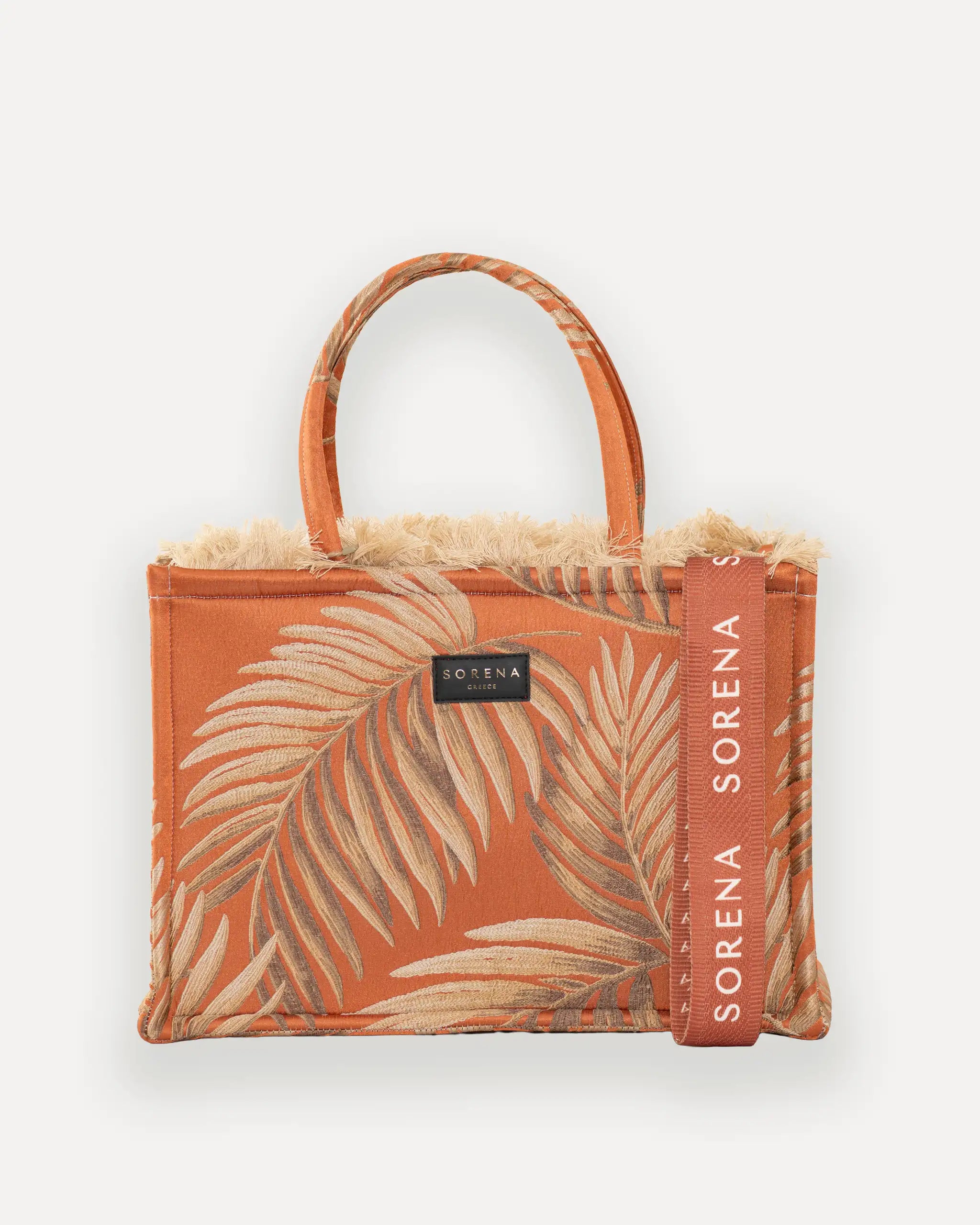 Frontansicht der Sorena Greece Large Tote Bag – tropisches Muster in warmen Tönen, Fransen, Label und vertikales Branding sichtbar, hochwertige shopper tasche damen schweiz mit Designfokus.