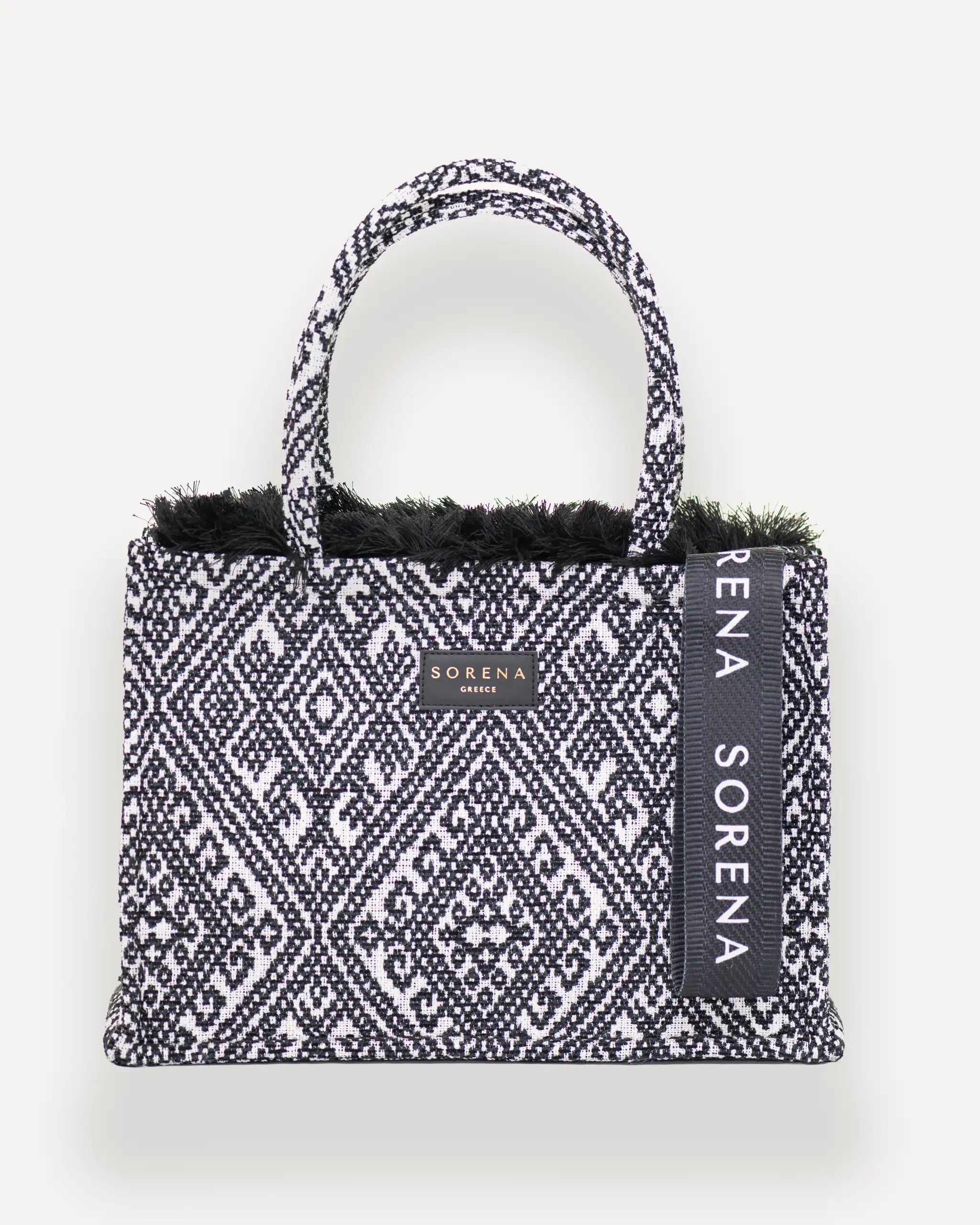Frontansicht der Sorena Greece Medium Tote Bag – schwarz-weißes geometrisches Muster, Fransen, Label und vertikales Branding sichtbar, hochwertige shopper tasche damen schweiz mit Designfokus.