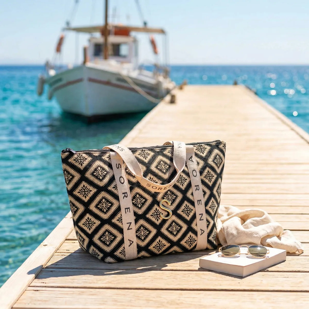 Traveller Bag von Sorena Greece auf einem Holzsteg am Meer mit
griechischem Segelboot im Hintergrund – handgefertigte Reisetasche
mit geometrischem Jacquard-Muster und SORENA-Tragegurten