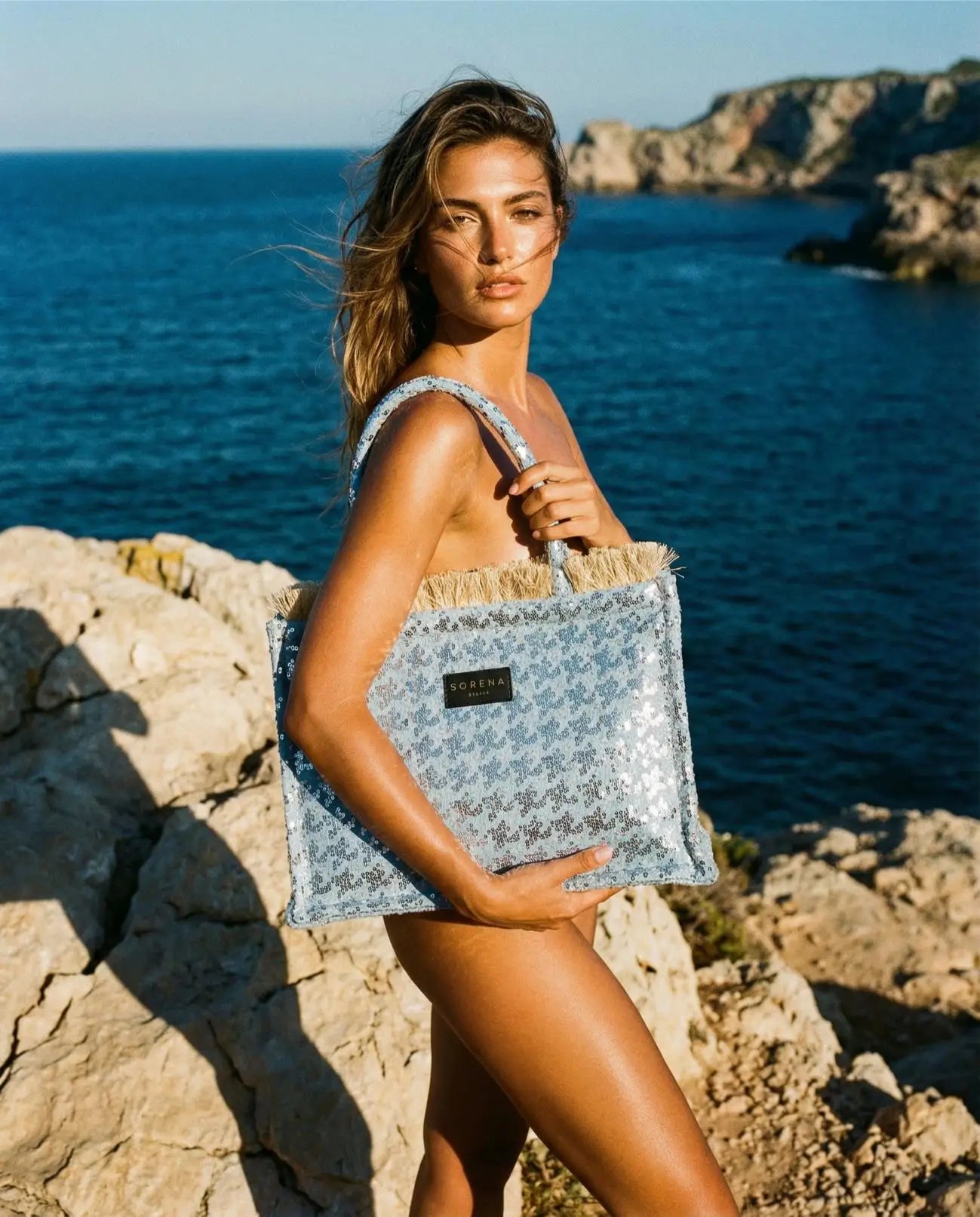 Sorena Greece Tritiani Medium Tote Bag mit Model am Meer in Frontansicht Micro Pailletten Silber irisierend Jean Jacquard Glitzereffekt handgefertigt.