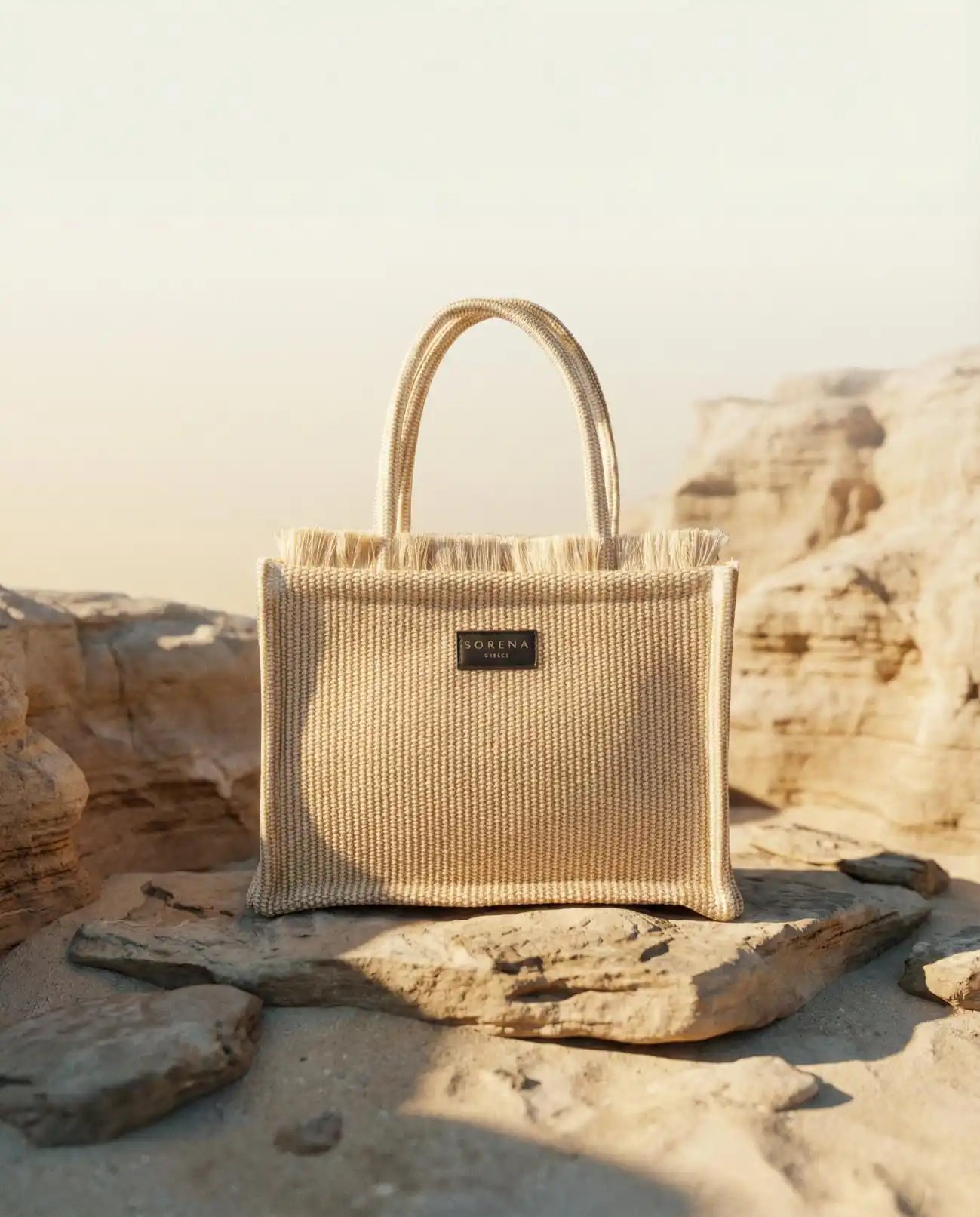 Sorena Greece Irida Medium Tote Bag auf Stein Frontansicht, Naturstroh Tote warmer Beige Ton handgefertigt Griechenland Cycladitissa Kollektion.