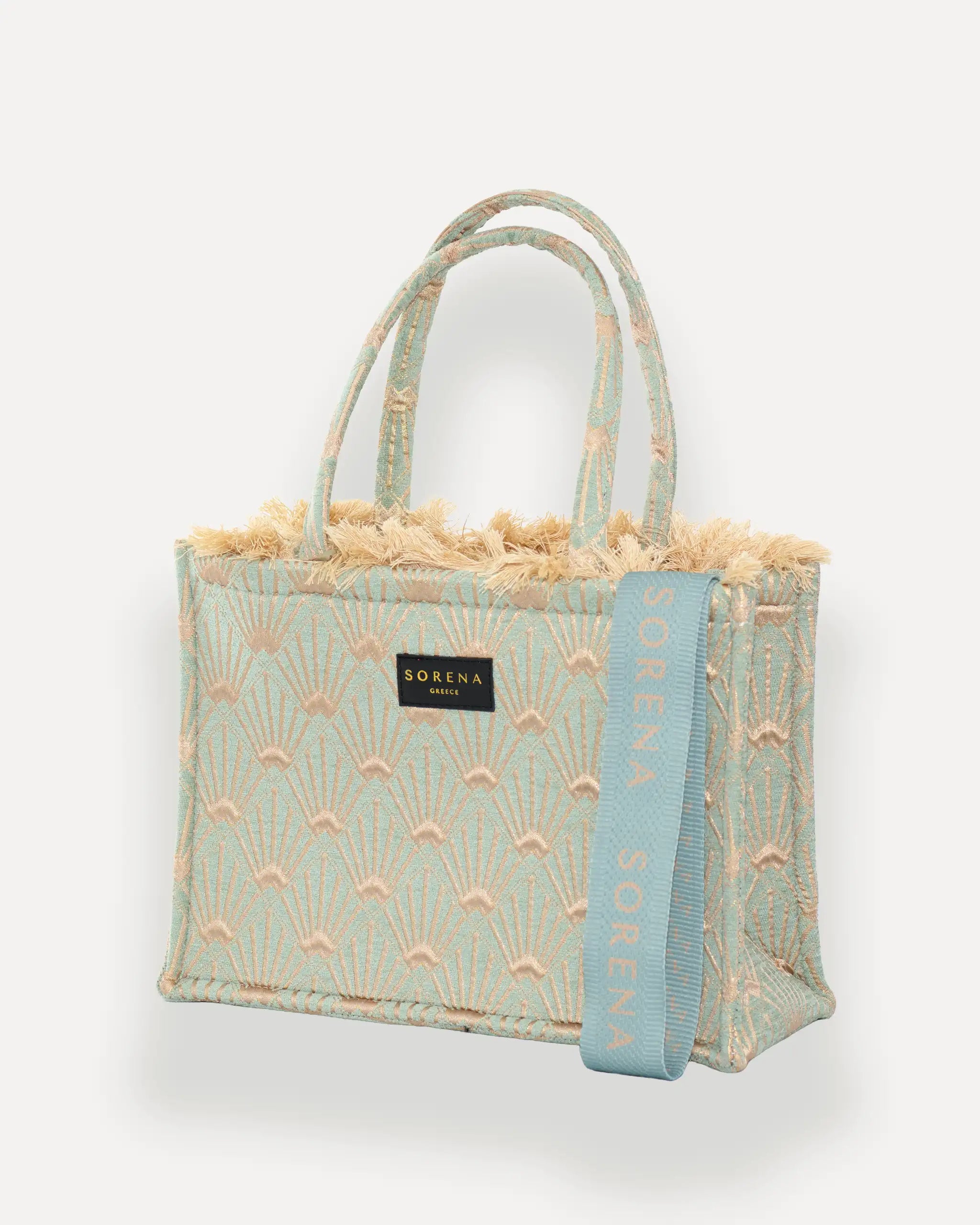 Sorena Greece Medium Tote Bag linksseitig getragen – elegante tote bag mit Fransen und vertikalem „SORENA“-Band, ideal als shopper bag für City-Looks, tote bag beige mit sommerlichem Charakter.
