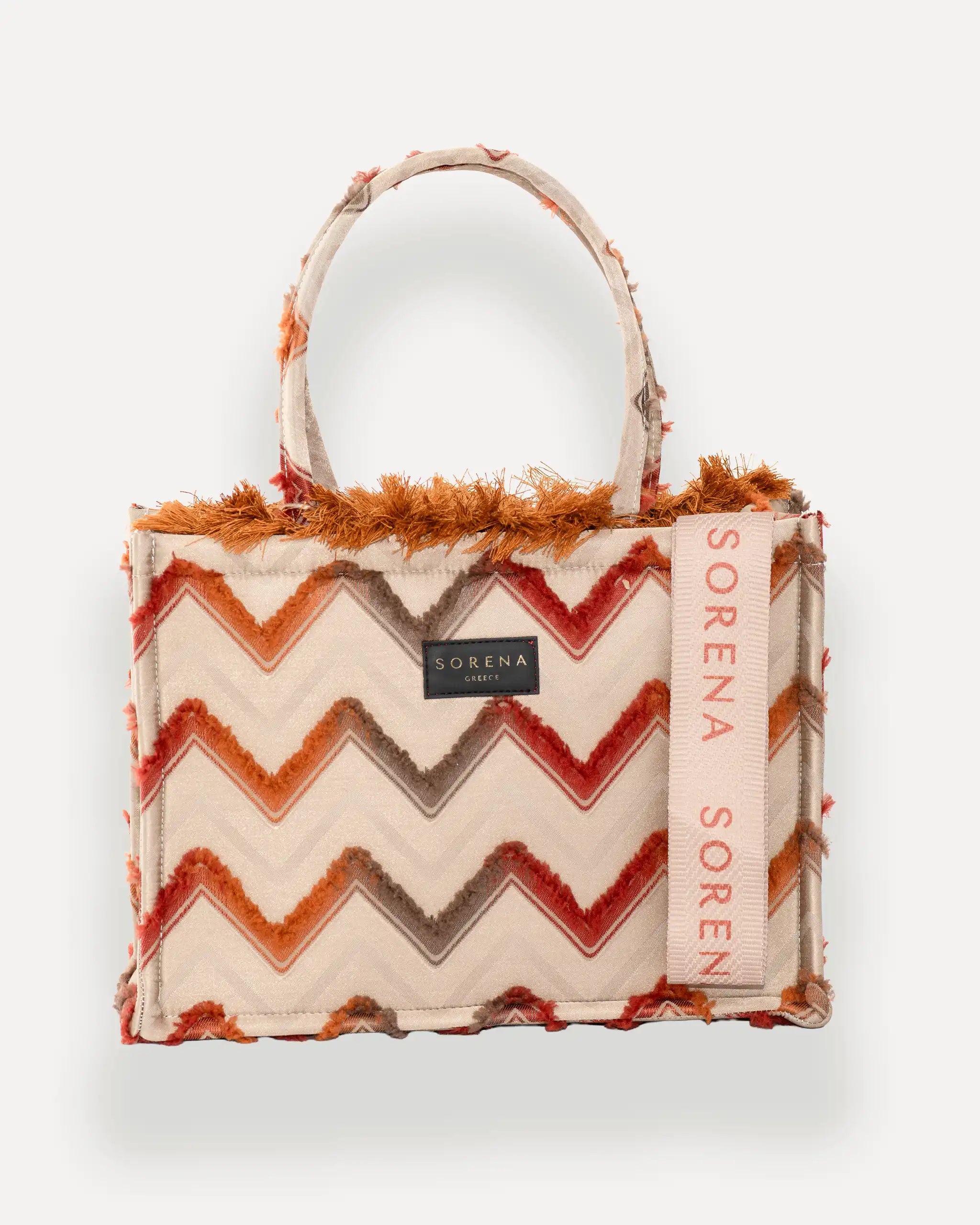 Frontansicht der Sorena Greece Medium Tote Bag – Zickzack-Muster in warmen Tönen, Fransen, Label und vertikales Branding sichtbar, hochwertige shopper tasche damen schweiz mit Designfokus.