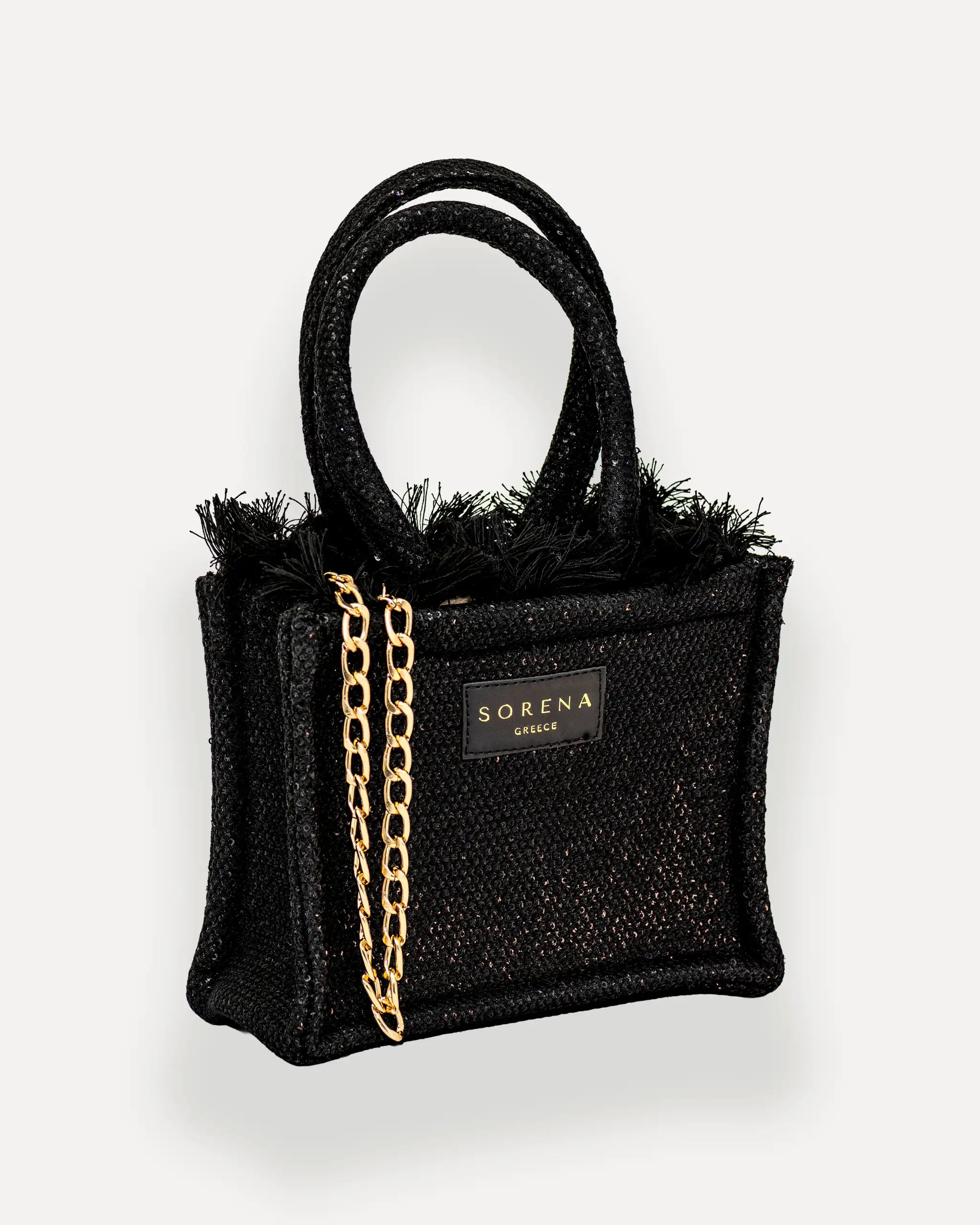 male Model mit Sorena Greece Mini Bag rechtsseitig getragen – kompakte umhängetasche damen in Schwarz, crossbody tasche mit Fransen und goldener Kette, bags schweiz mit Statement-Charakter.